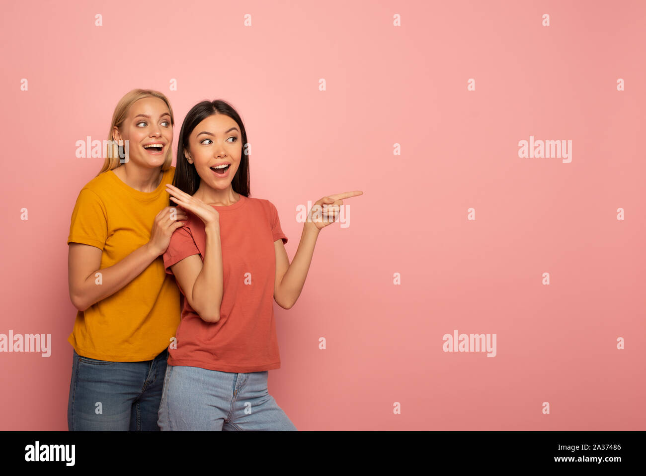 Zwei Mädchen zeigt an etwas. Erstaunt Ausdruck Gesicht. Rosa Hintergrund mit leeren Platz für Ihren Text Stockfoto