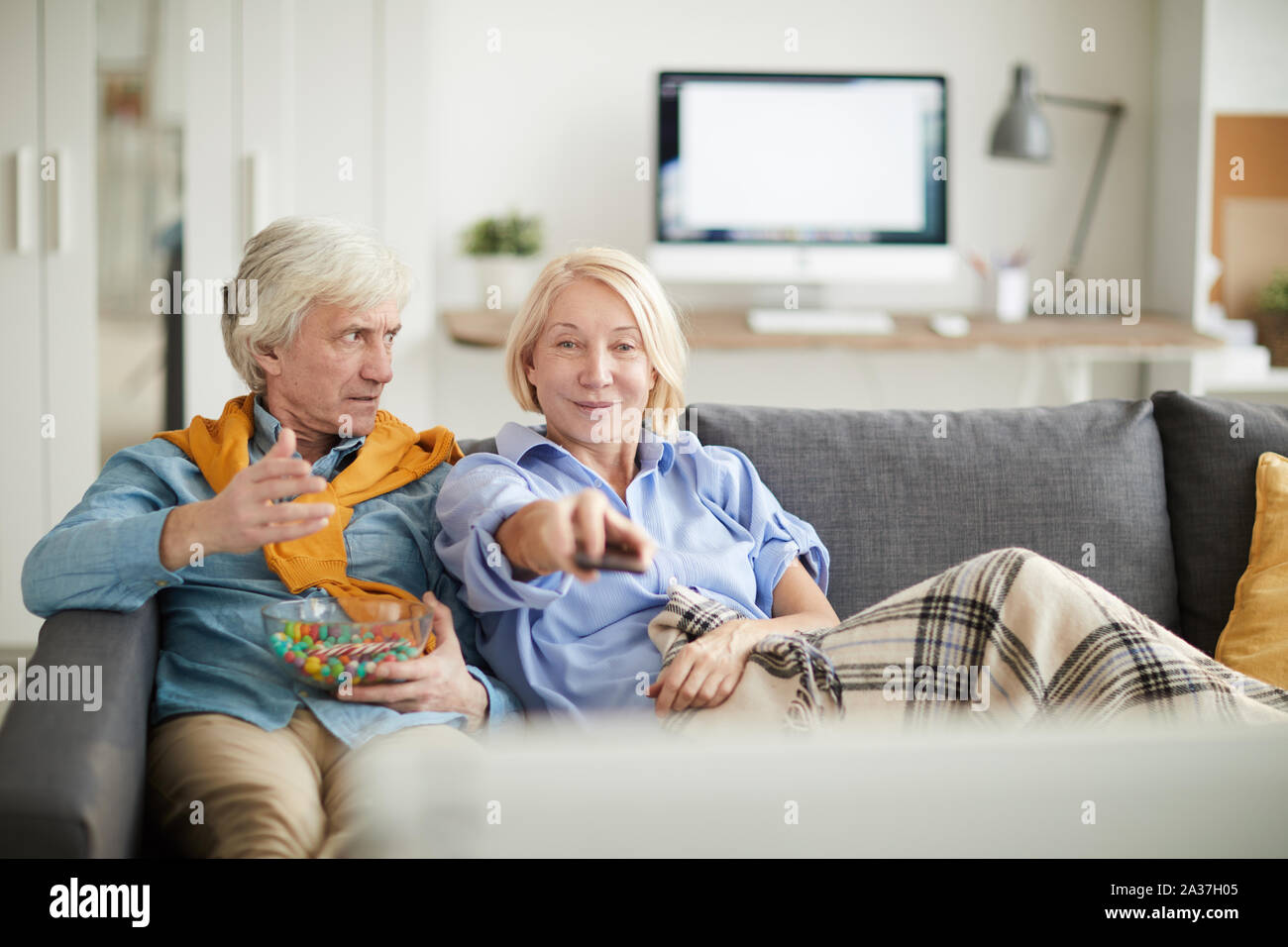Portrait des modernen Senior paar TV zusammen beobachten, auf frustrierte Ehemann an Frau Schaltkanäle, kopieren Raum Suche Fokus Stockfoto