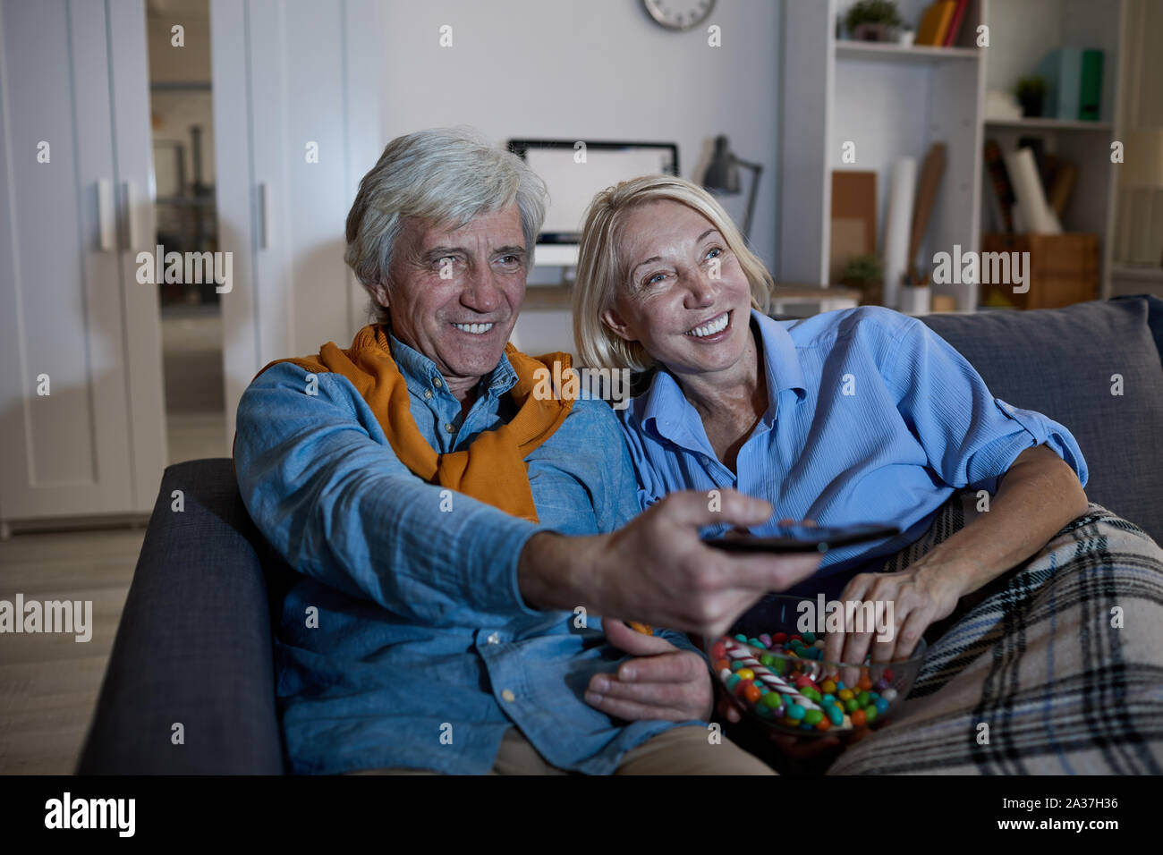 Portrait von lächelnden Senior paar Fernsehen zusammen sitzen auf komfortablen Couch im dunklen Raum, kopieren Stockfoto