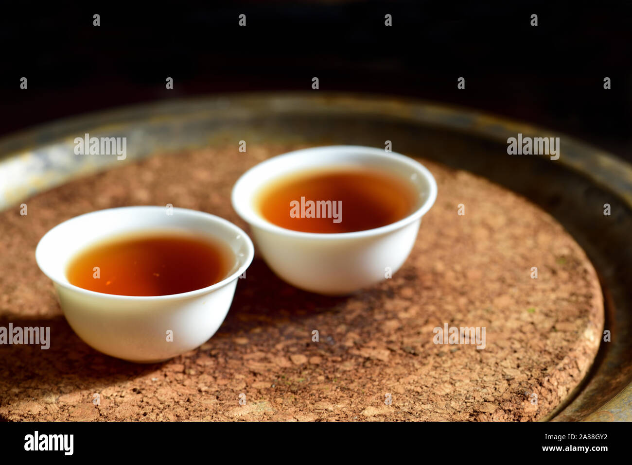 Nahaufnahme von zwei kleine Chinesische Weiße Tasse mit schwarzem Kaffee auf einem Teller mit Kork Platte und dunklen Hintergrund an einer chinesischen Teezeremonie Stockfoto