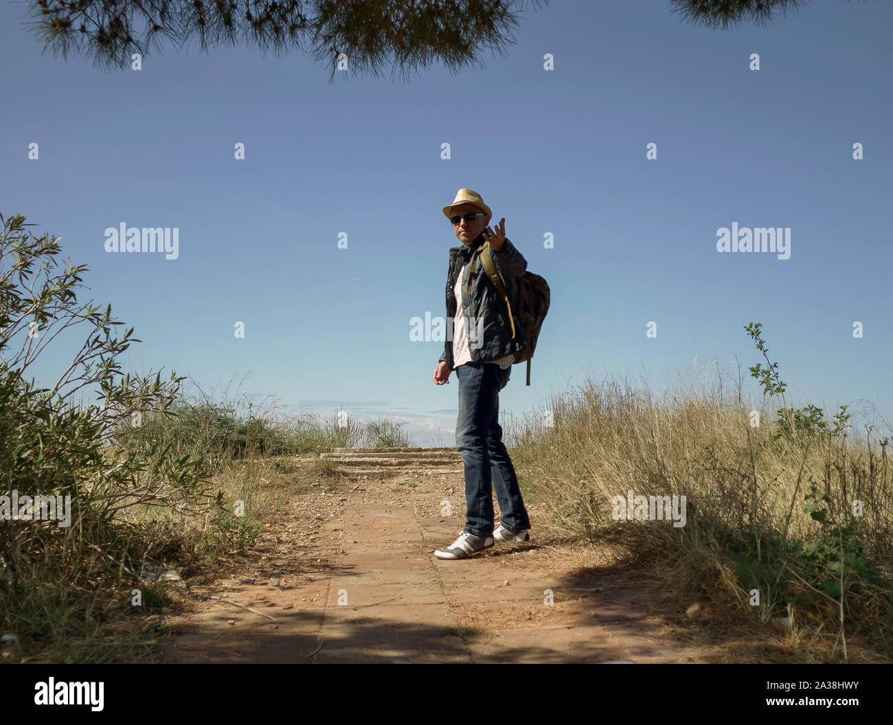 Ein Mann Reisender in einen Hut und mit einem Rucksack steht auf der Aussichtsplattform auf einem Hügel und hält seine Hand. Follow me Stockfoto