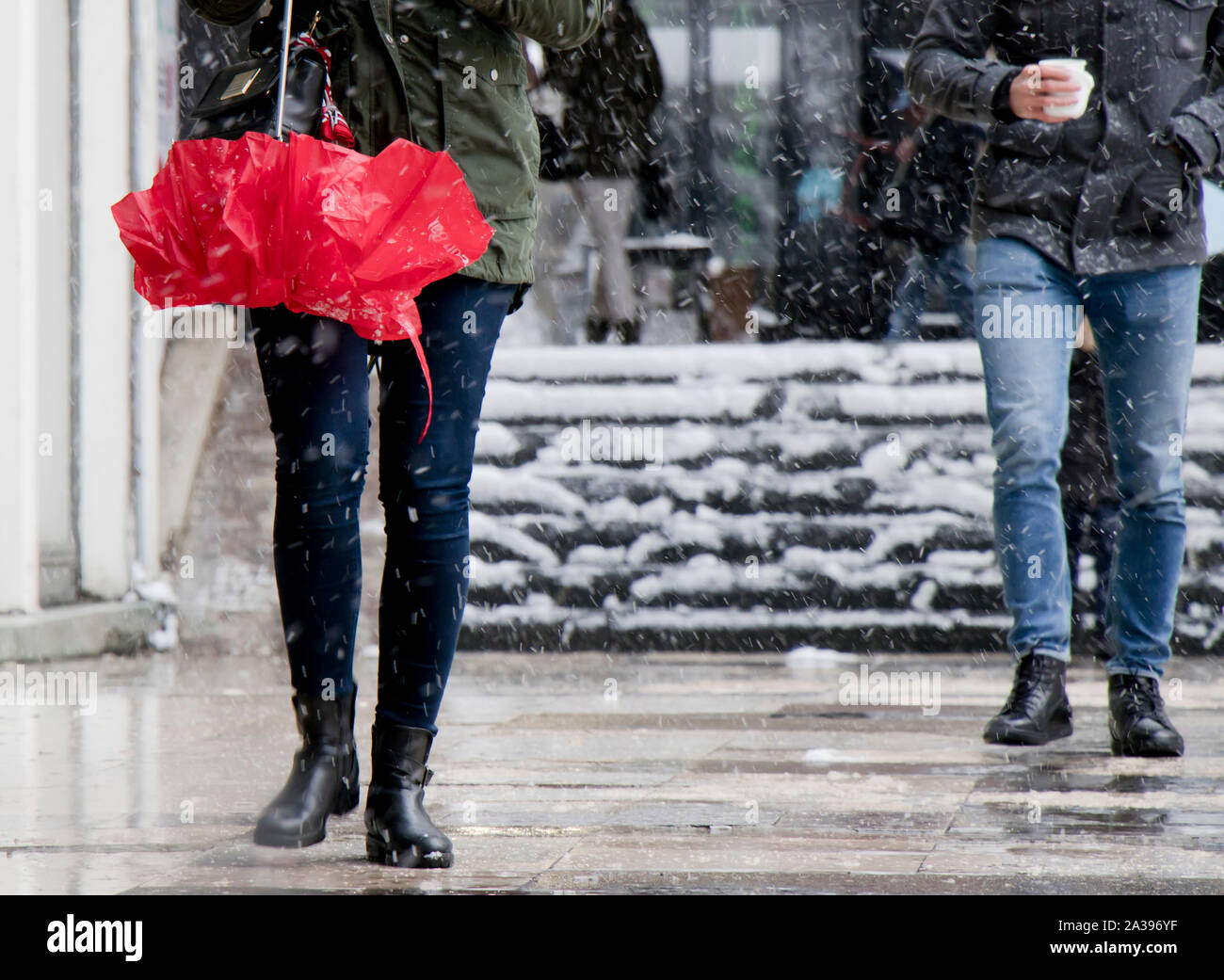 Junge Menschen zu Fuß auf verschneite Stadt Bürgersteig, Regenschirm und warme Getränke, von der Taille abwärts Stockfoto