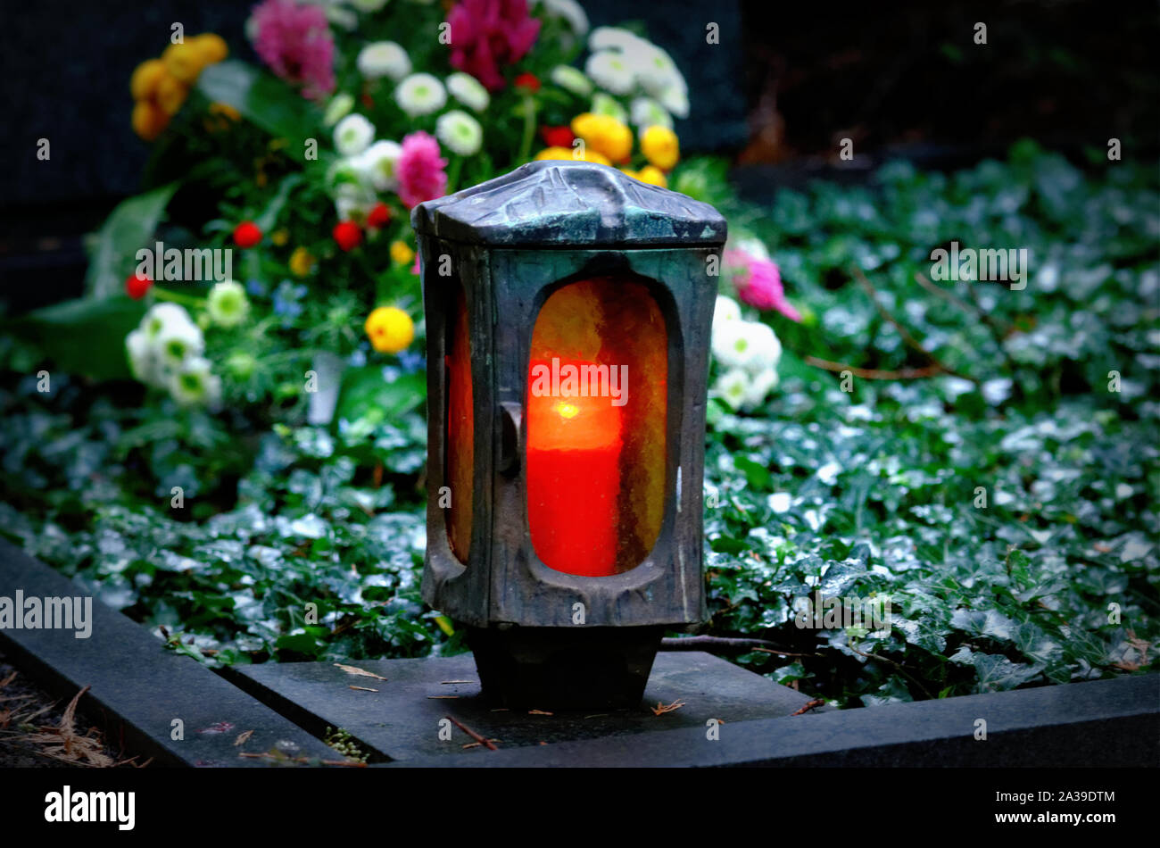 Grab Licht mit brennenden Kerze auf einem Grab mit Blumen an einem Herbstabend Stockfoto