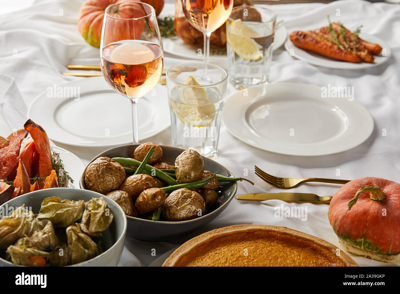 Gebackene Kartoffel und Physalis in der Nähe von Gläsern mit Rose Wein und Zitronensaft Wasser auf weißen Tischdecke Stockfoto