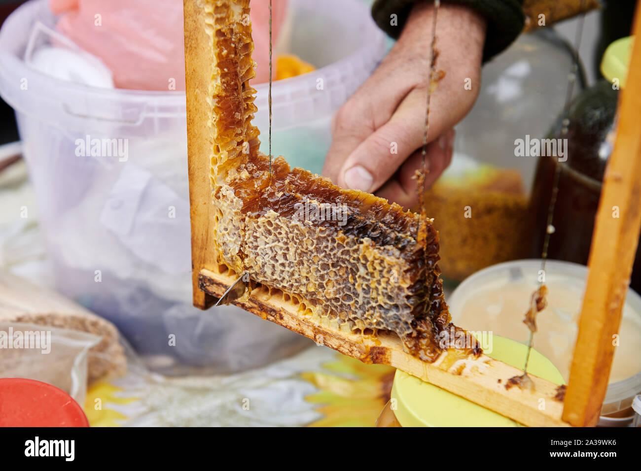 Hand des Menschen schneidet ein köstliches Stück Wabe mit dem Messer. Verkauf von hausgemachten Honig auf dem Markt. Degustation Nahaufnahme. Honey Farm. Stockfoto