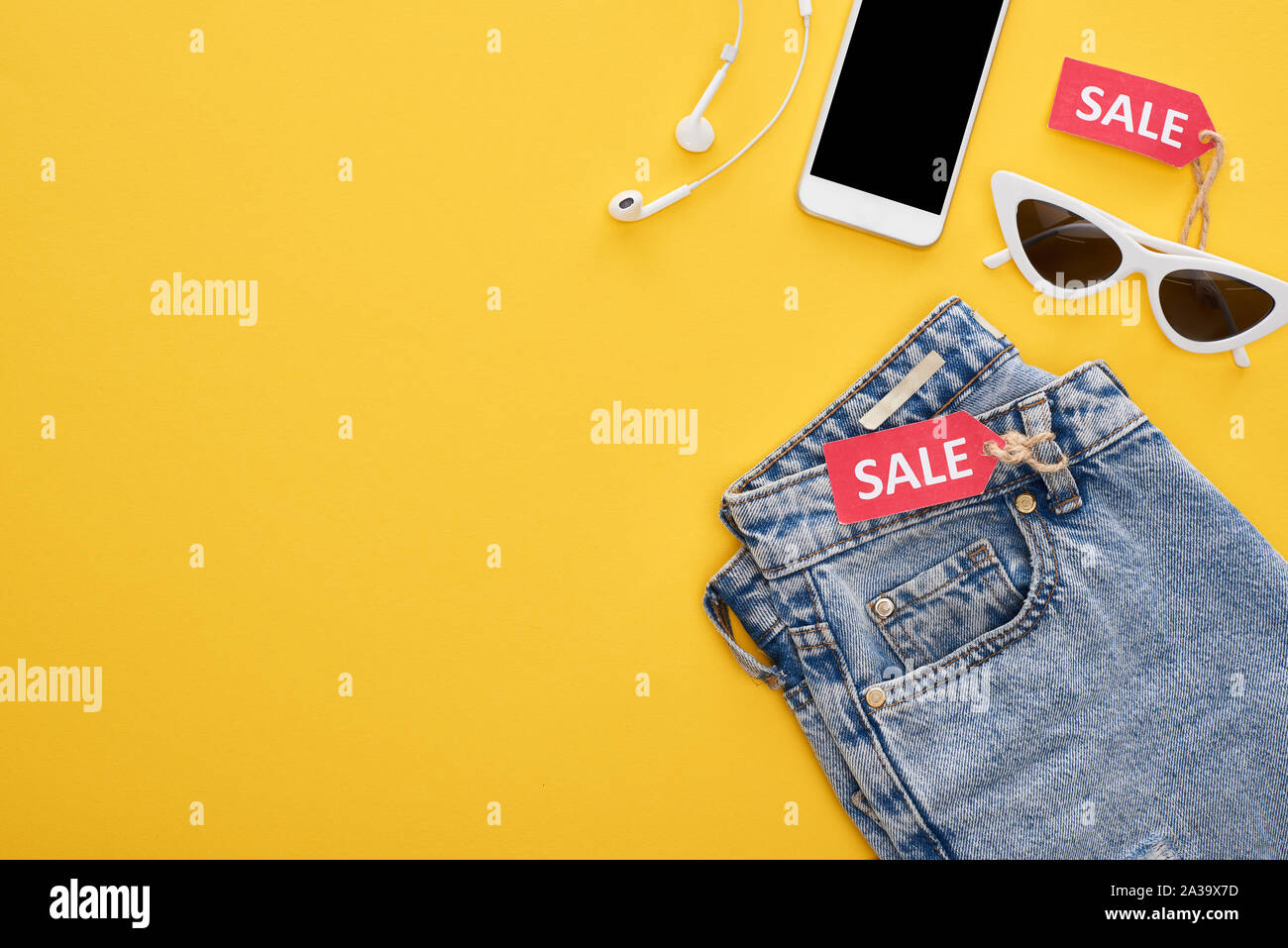 Blick von oben auf die Jeans, Gläser und Smartphone mit Ohrhörer mit Verkauf Etiketten auf gelbem Hintergrund Stockfoto