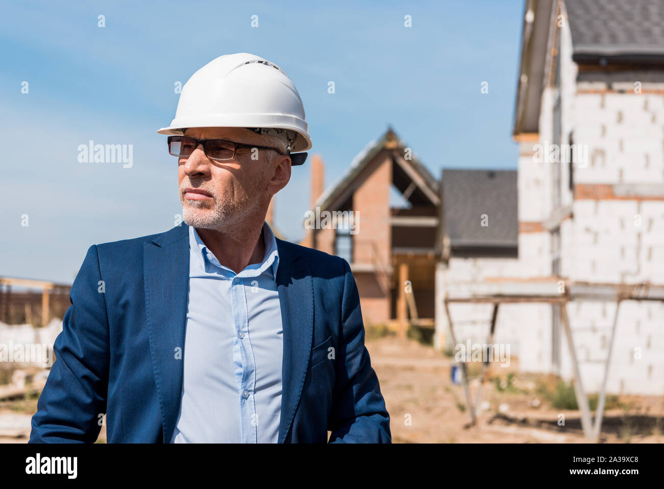 Reifen und bärtigen Geschäftsmann in Anzug und Helm in der Nähe von Gebäuden Stockfoto