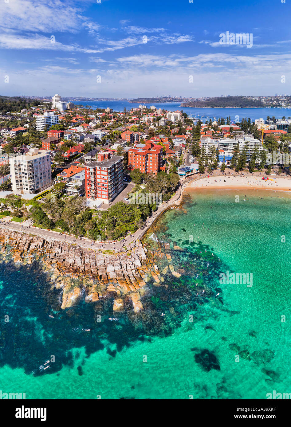 Berühmten Manly Beach in Sydney Northern Beaches mit weit entfernten Hafen von Sydney und CBD Türme über Horizont in Antenne vertikale Ansicht von pazifischen Gewässern surfen Stockfoto