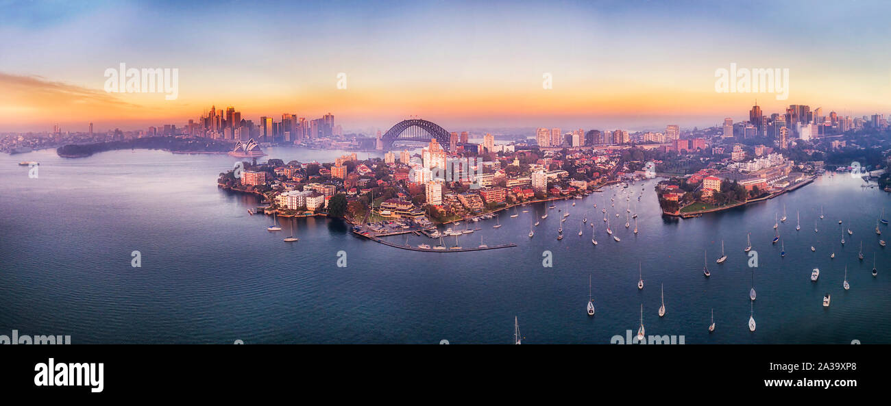 Breite Antenne Panorama über die Bucht aus Kirribilli mit Marina und Yachten im Hafen von Sydney mit Blick auf die große Stadt CBD Wahrzeichen bei Sonnenaufgang mit goldenen Horiz. Stockfoto