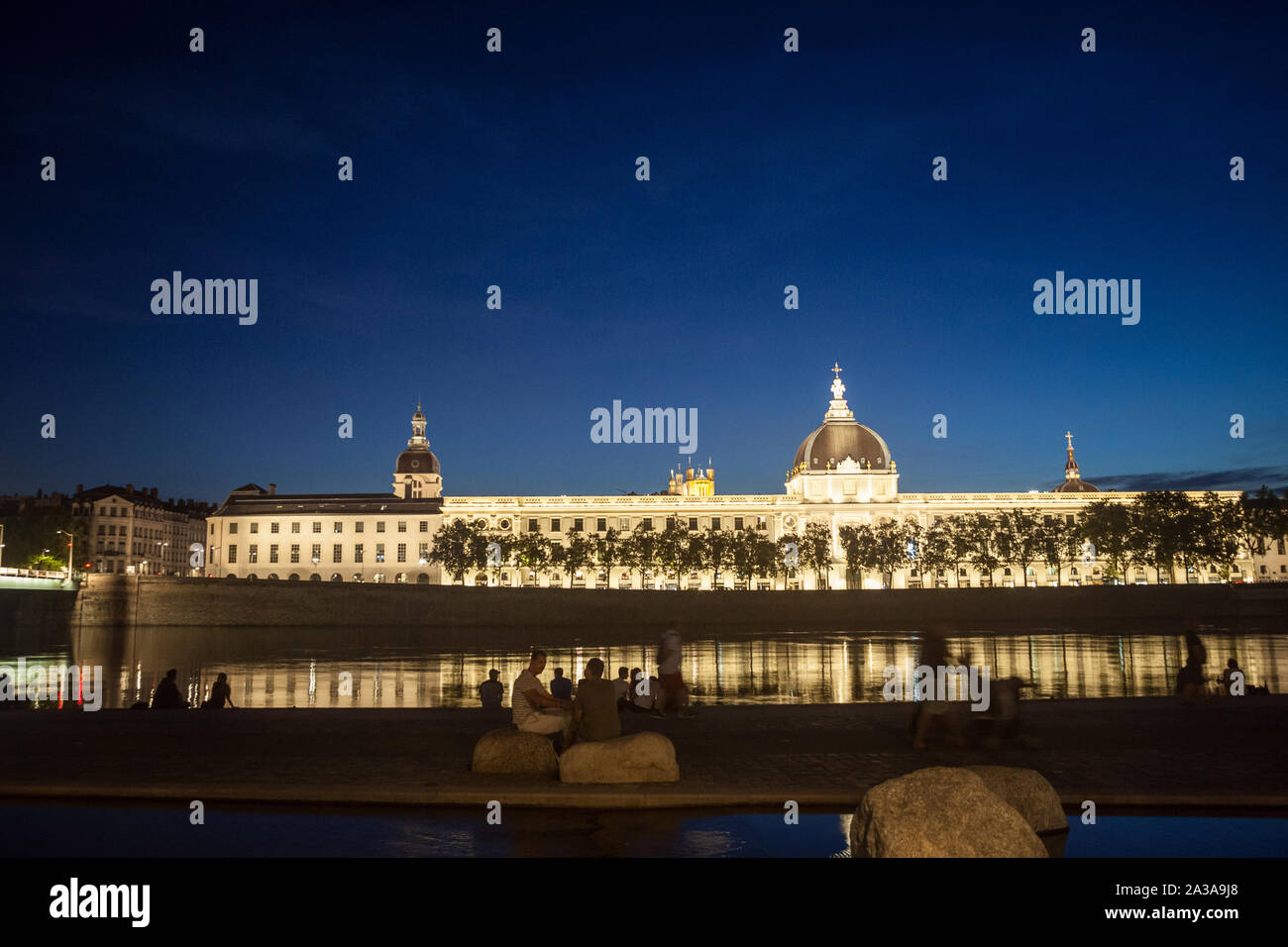 LYON, Frankreich - 18. JULI 2019: Franzosen sitzen am Ufer des Quais de Rhone, gegenüber Hotel Dieu, eines der wichtigsten Denkmäler der Stadt w Stockfoto