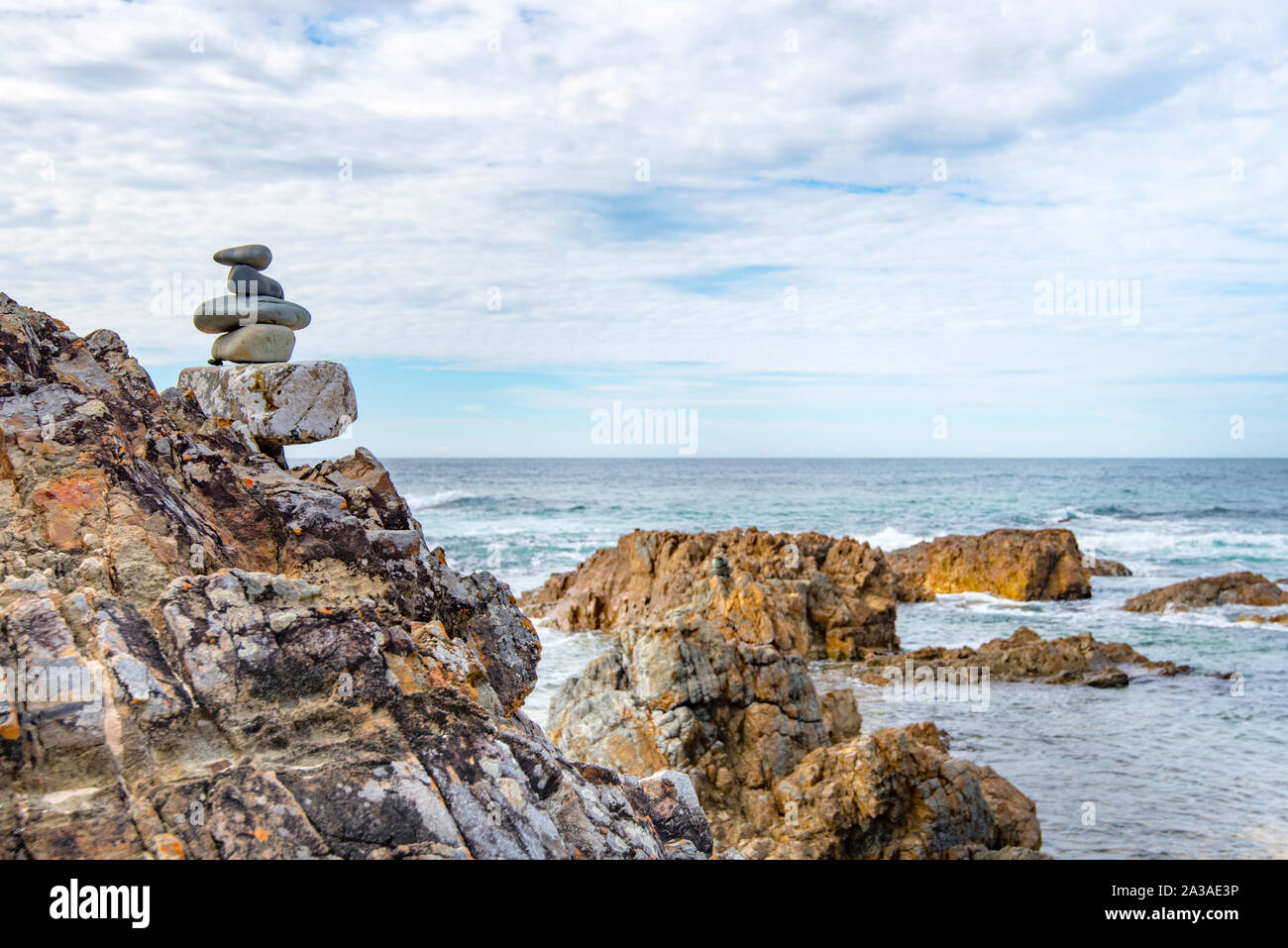 Eine Nahaufnahme von einem Satz von glatte Steine vertikal gestapelt und auf einem großen Felsen neben eingehenden Surfen und das Meer in Australien ausgeglichen Stockfoto