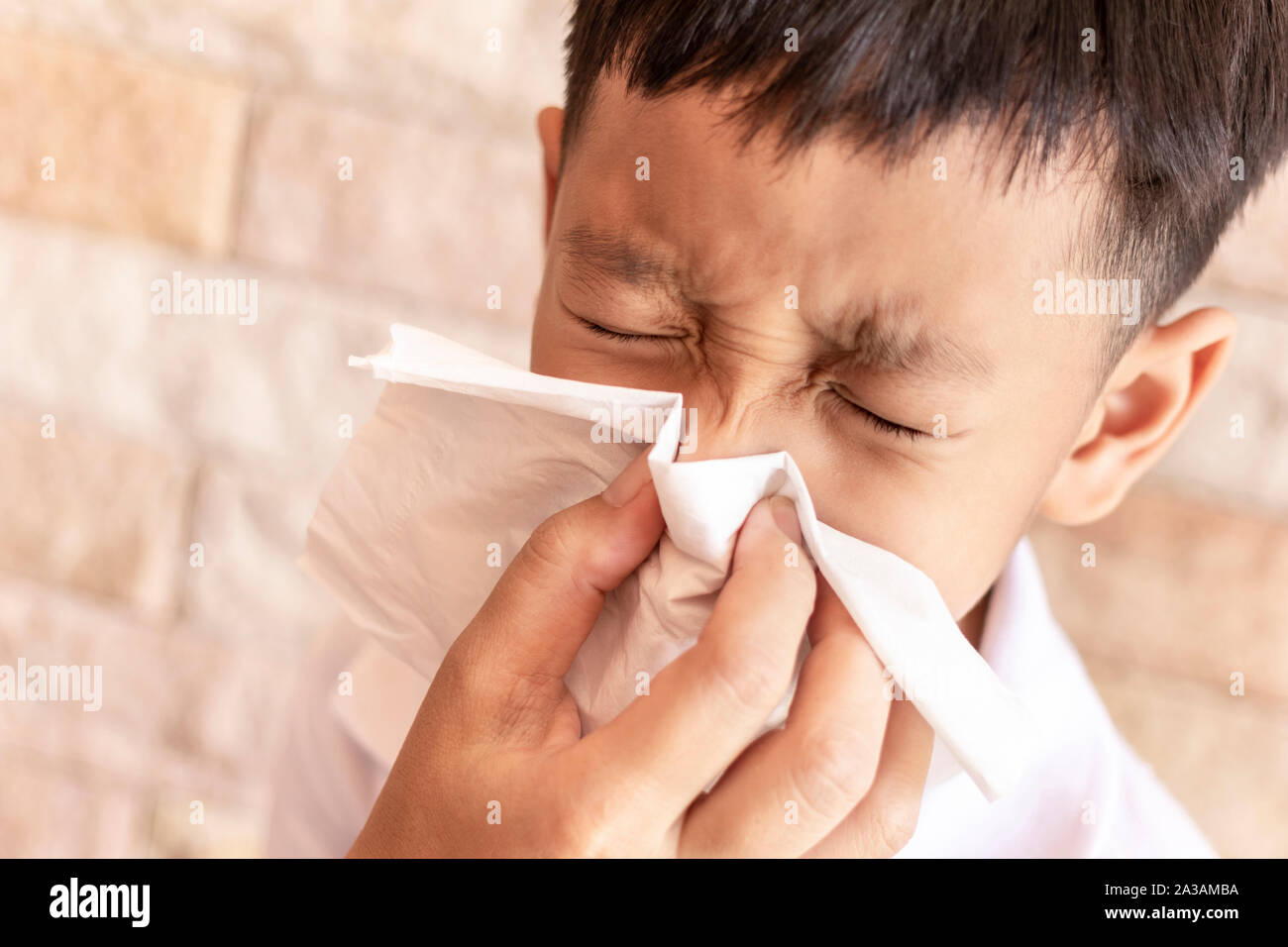 Eltern helfen, einem Kind die Nase in die Luft zu sprengen. Asiatische little boy blasen Nase mit einem Taschentuch zu Hause. Stockfoto