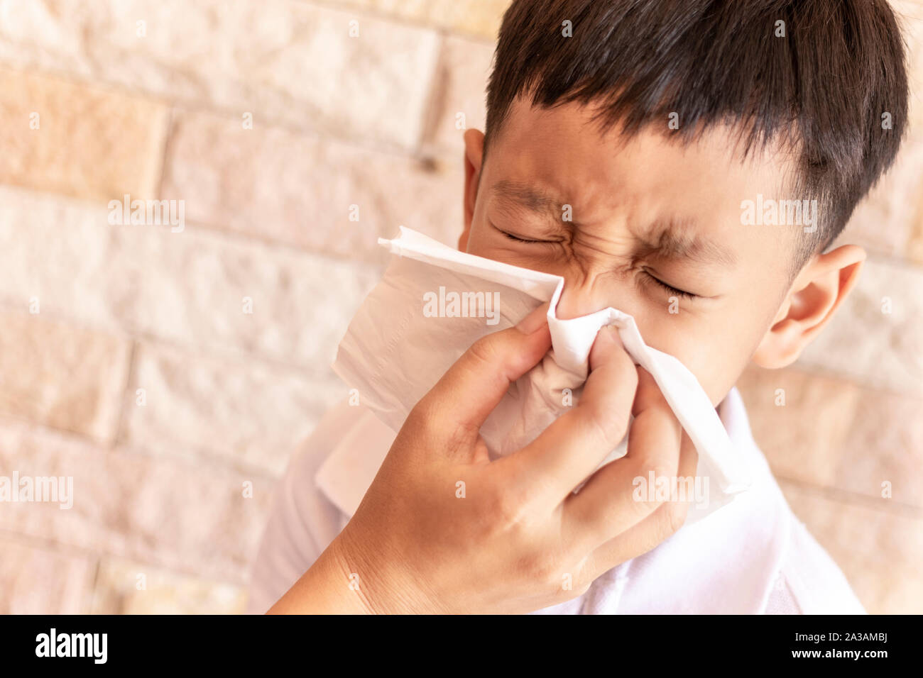 Eltern helfen, einem Kind die Nase in die Luft zu sprengen. Asiatische little boy blasen Nase mit einem Taschentuch zu Hause Stockfoto