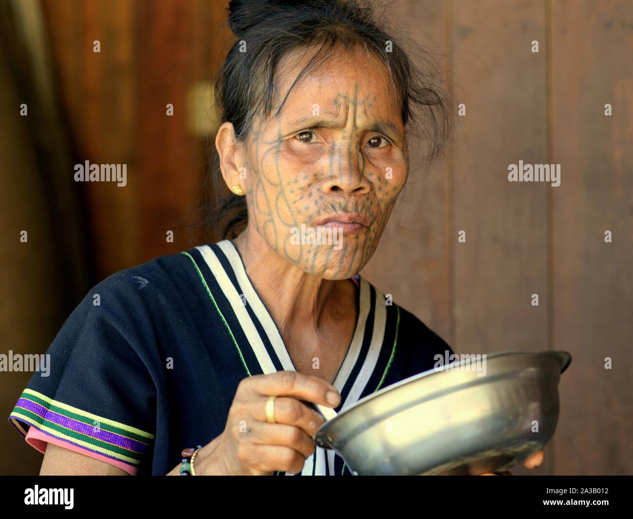 Im mittleren Alter Kinn Muun tribal Frau ('Spider Frau') mit klassischen Gesichtsbehandlung tattoo isst aus Edelstahl Schüssel und sieht in die Kamera. Stockfoto