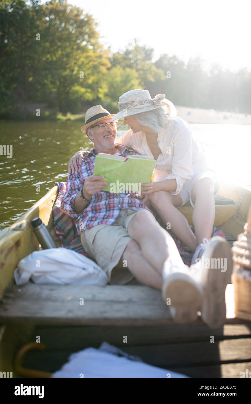 Frau umarmen Mann beim Chillen im Boot und Lesen Stockfoto