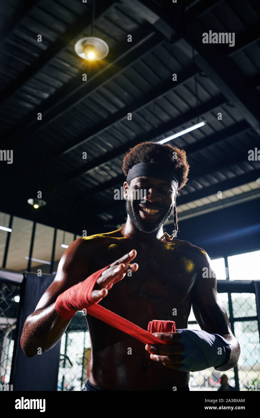 Lächelnd Schwarz Muay Thai Boxer wickeln Handgelenke mit Binde sie während der Schulung zu schützen. Stockfoto