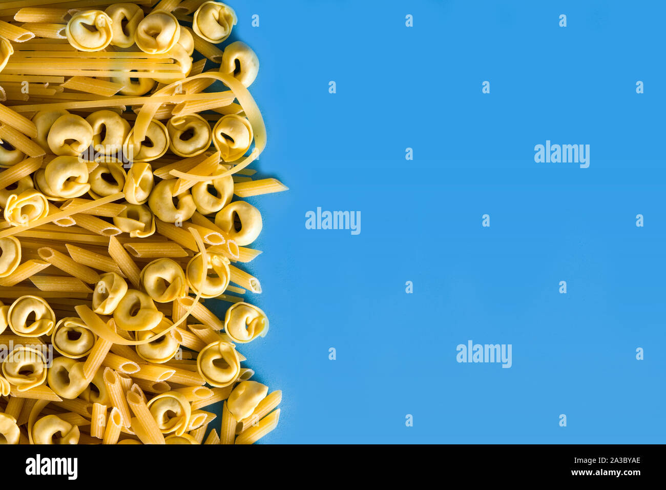 Verschiedene Arten von Pasta. Penne Pasta, Ravioli, Tortellini und capellini auf blauem Hintergrund Stockfoto