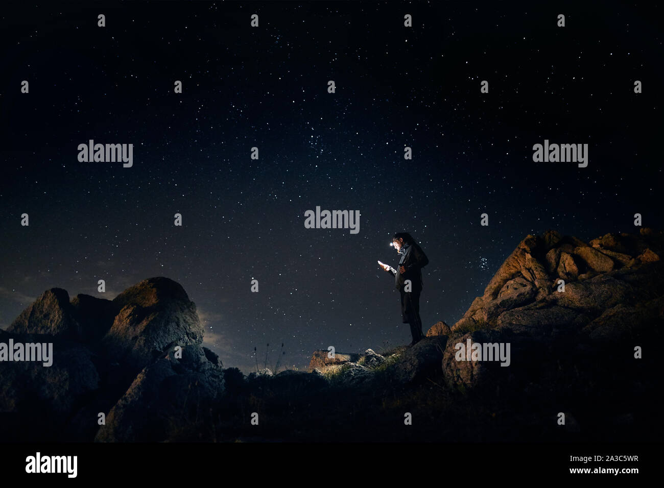 Der Mensch ist auf der Suche bei seinem Telefon mit seinem Kopf Licht am sternenklaren Nacht die Berge Stockfoto