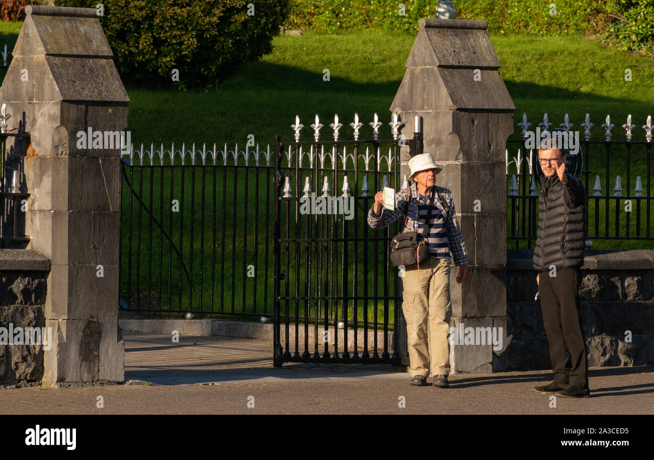 Alte älterer Frauen verloren touristische Fragen nach dem Weg an der Kirche Zaun in weiches Abendlicht verwirrt. Stockfoto
