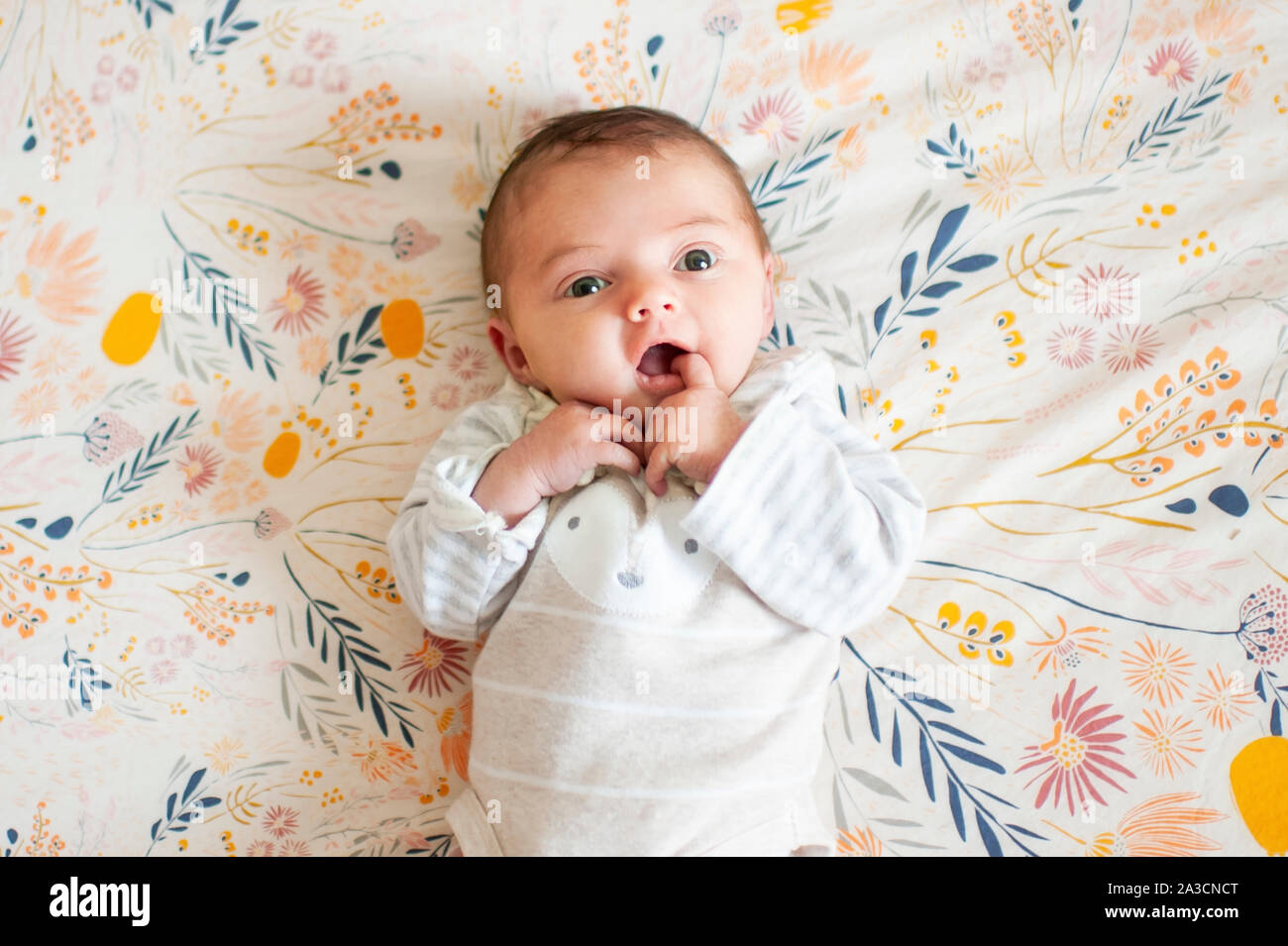 Neugeborenes Baby girl looking up mit niedlichen Ausdruck mit dem Finger im Mund Stockfoto