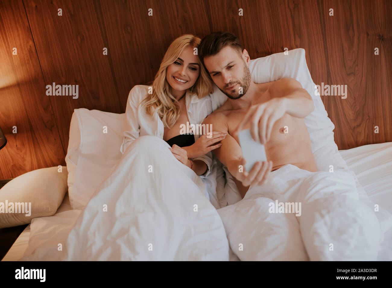 Glückliches Paar im Bett zu Hause liegen und ein Mobiltelefon verwenden Stockfoto