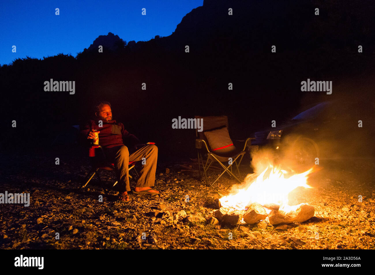 Das sitzen an einem leuchtenden Lagerfeuer mit einem Bier in der Wüste bei Nacht, Freiheit Camping in schöner Natur, Valbona Tal, Albanien Stockfoto