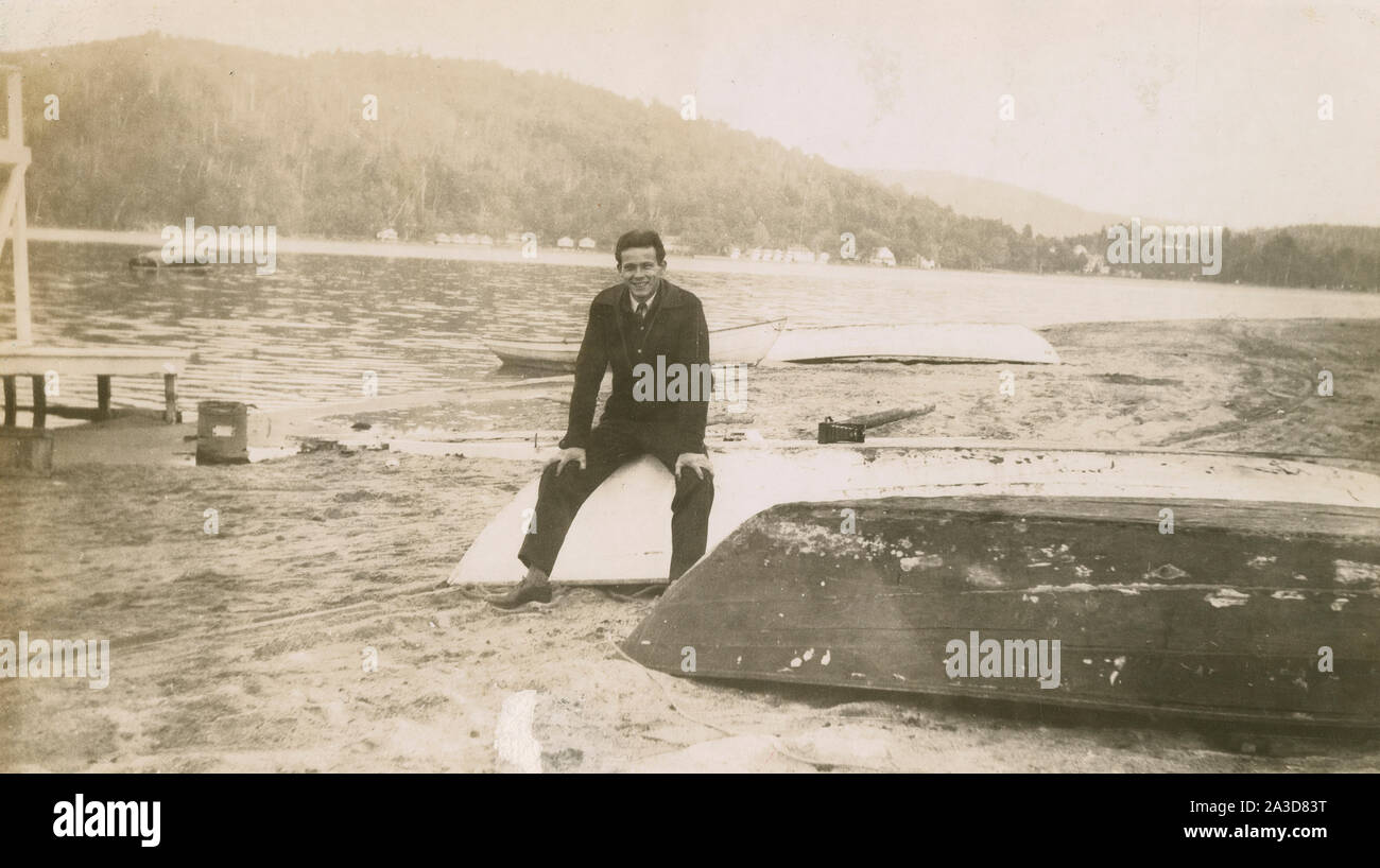Antike Oktober 12, 1945 Foto, Mann auf Ruderboote sitzend auf dem Strand in der Nähe des Bungalow Dorf am Newfound Lake, New Hampshire. Quelle: original Foto Stockfoto