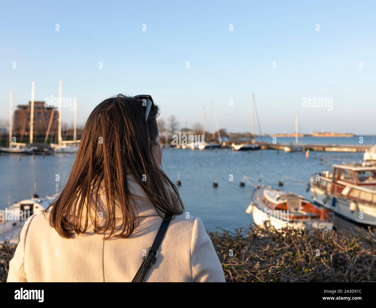 Schicke Frau schaut in einen Hafen mit Booten während eines Sonnenuntergangs Stockfoto