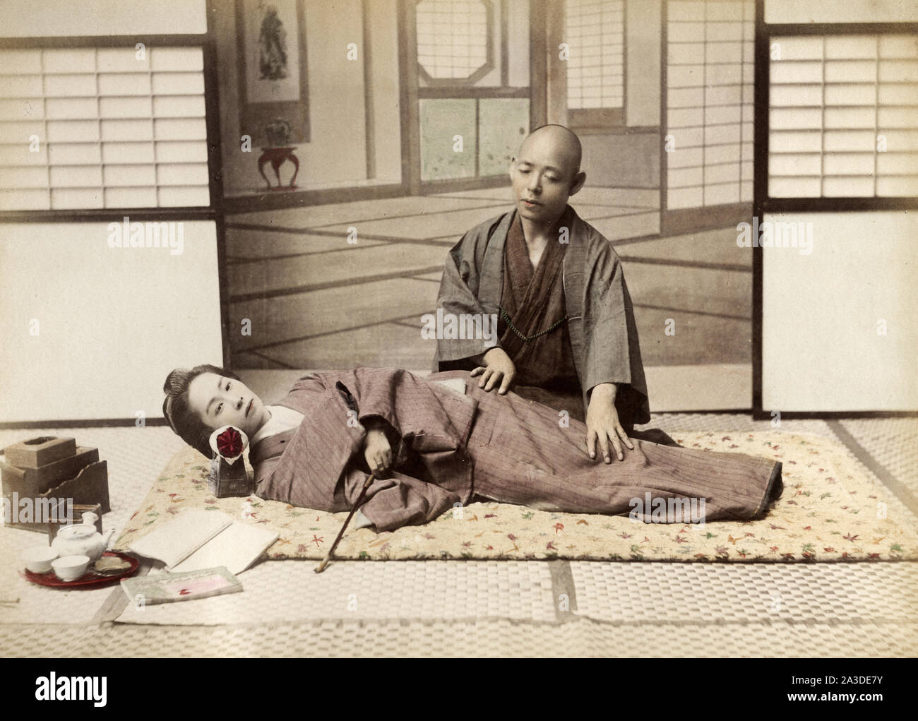 Vintage-Portraitfoto aus dem 19. Jahrhundert, bei dem eine junge Japanerin von einem blinden Masseur massiert wird, anma, Japan. Stockfoto