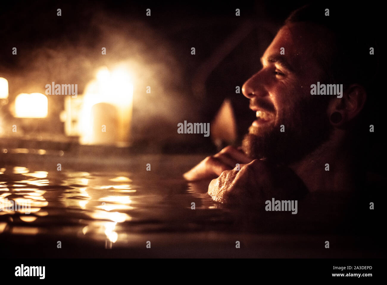 Mann in der Tür aus Whirlpool lächelt mit Kerzenlicht und Dampf Stockfoto