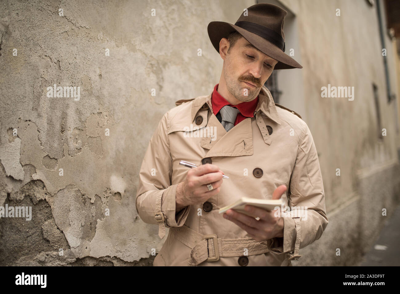 Detektiv schreiben auf einem Notebook während stadning in der Nähe einer alten Mauer Stockfoto