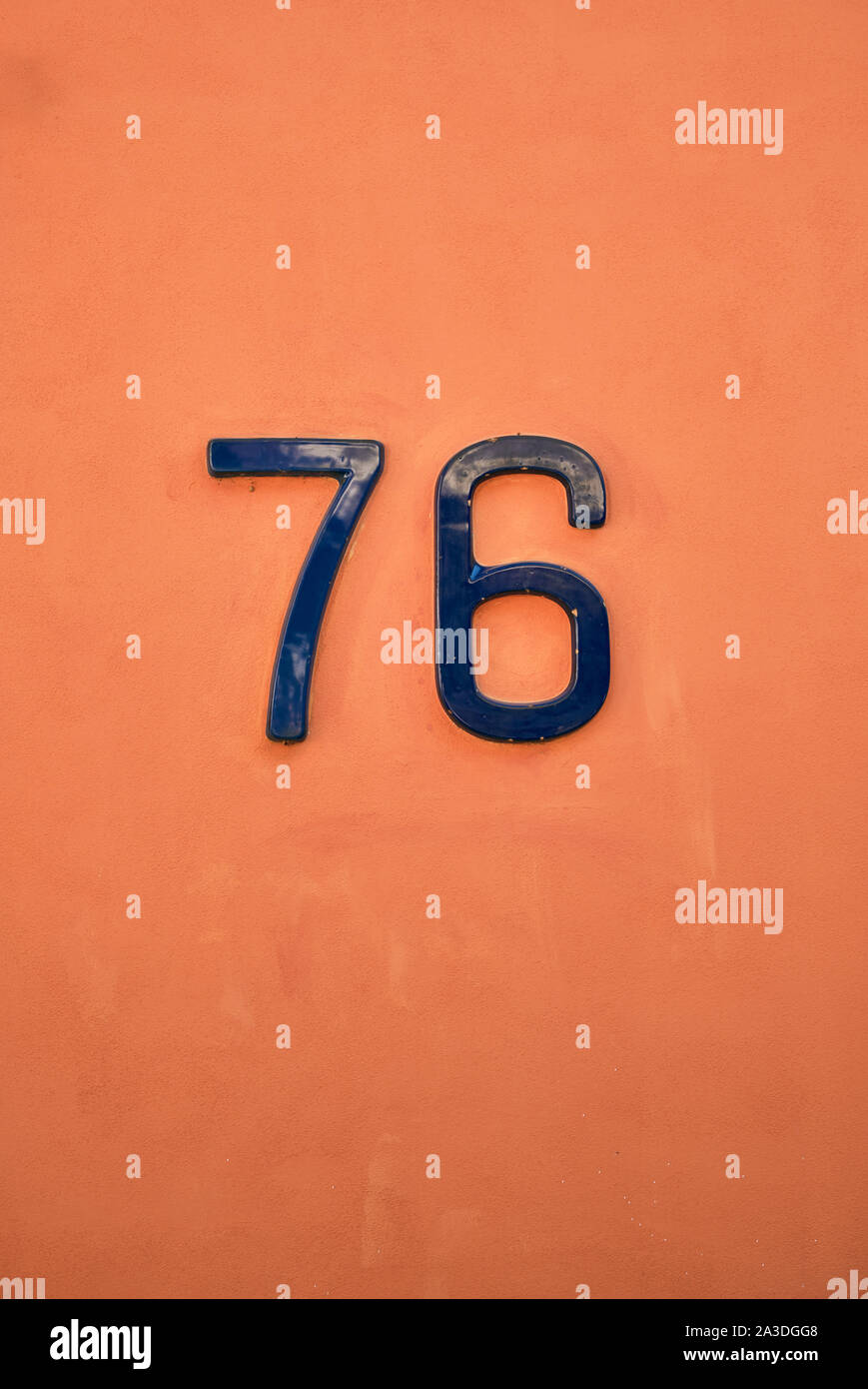 Lackiertes Metall Hausnummer 76 auf glatten orange Beton Wand von Gebäude Stockfoto