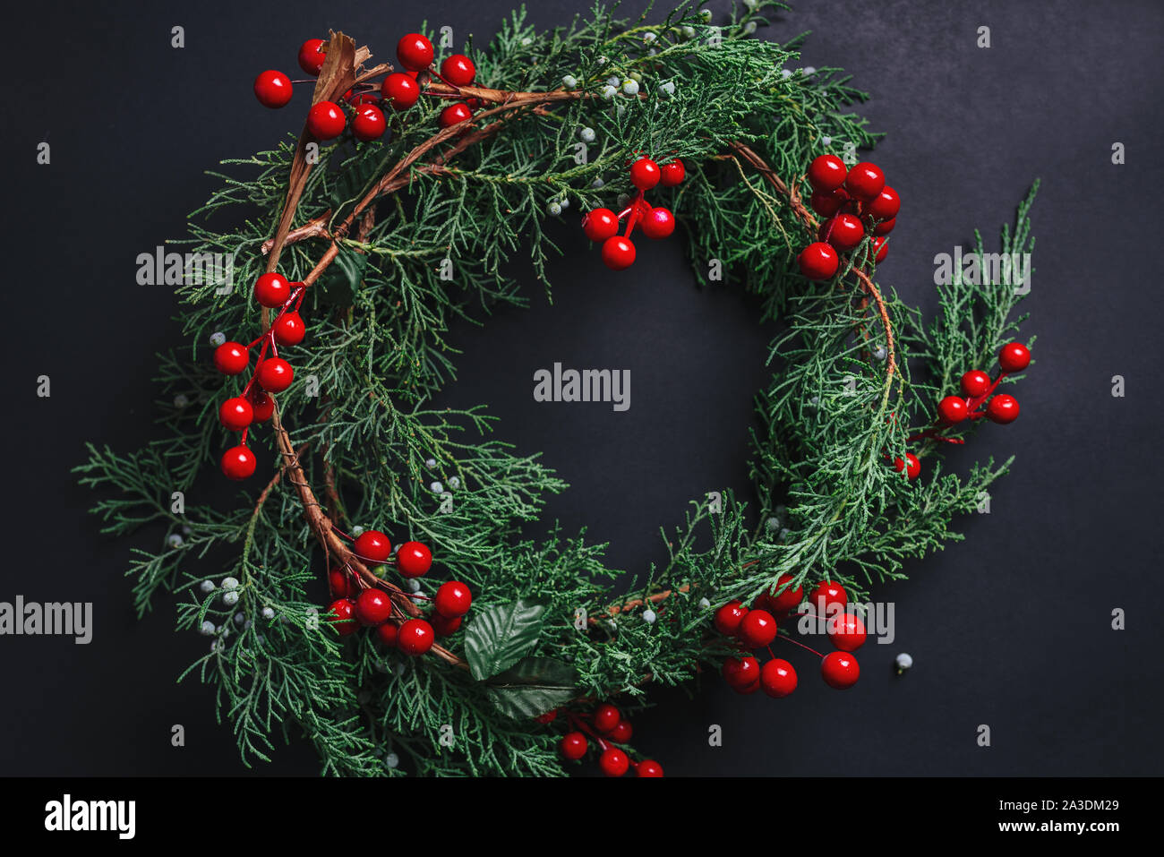 Weihnachten Kranz detail von Evergreen und Beeren auf dunklem Hintergrund. Nandian Netzwerk grüner Zweig und rustikalen Krone. Flach. Weihnachten Konzept. Stockfoto