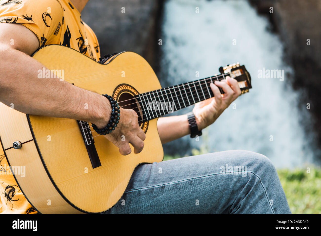 Closeup Schoß eines jungen Mannes an, Gitarre zu spielen, im Freien in einer natürlichen Landschaft Stockfoto