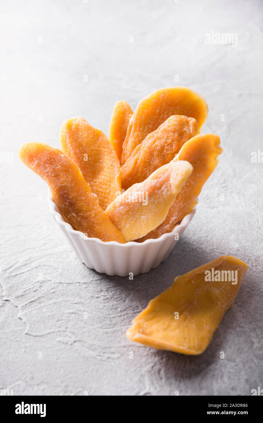 Entwässert und getrocknet mango Chips in Weiß Schüssel auf konkrete hellen Hintergrund. Close Up. Stockfoto
