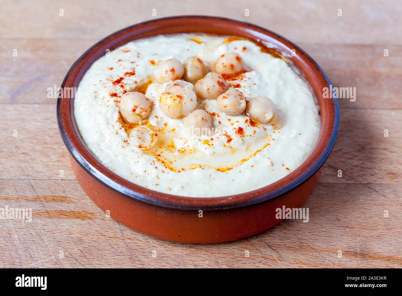 Stil Houmous dip gekrönt mit Paprika und Kichererbsen in Terrakotta Teller Stockfoto