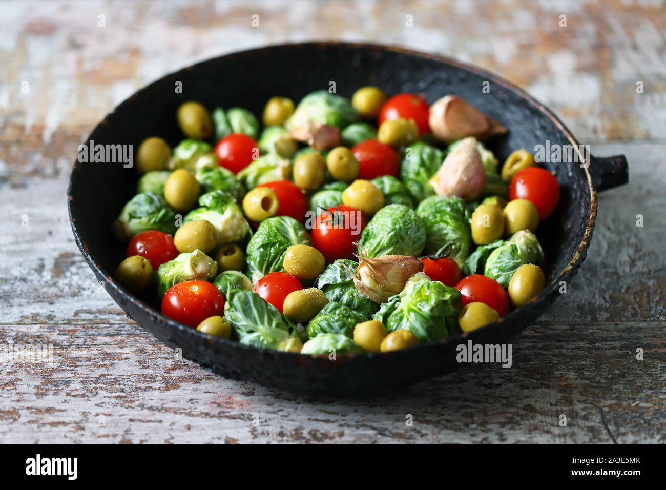 Rosenkohl in einer Pfanne mit Tomaten, Knoblauch und Oliven vor dem Backen. Gesundes Essen. Vegane Ernährung. Gemüse Pfanne. Stockfoto