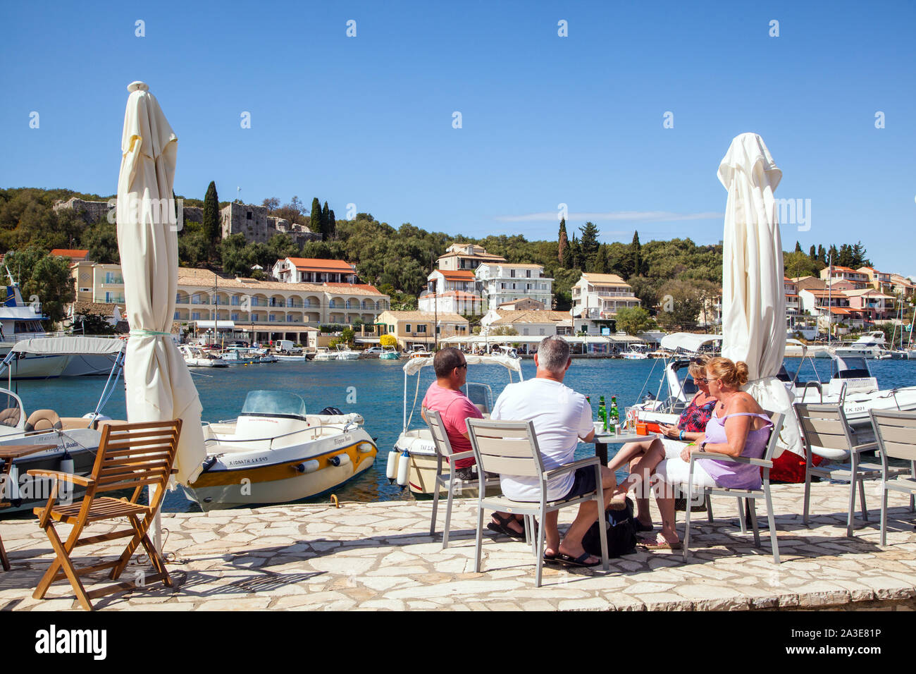 Leute, Touristen und Urlauber Essen und Trinken in den Cafes und Bars rund um den Hafen an der griechischen Ferienort Kassiopi Korfu Griechenland Stockfoto