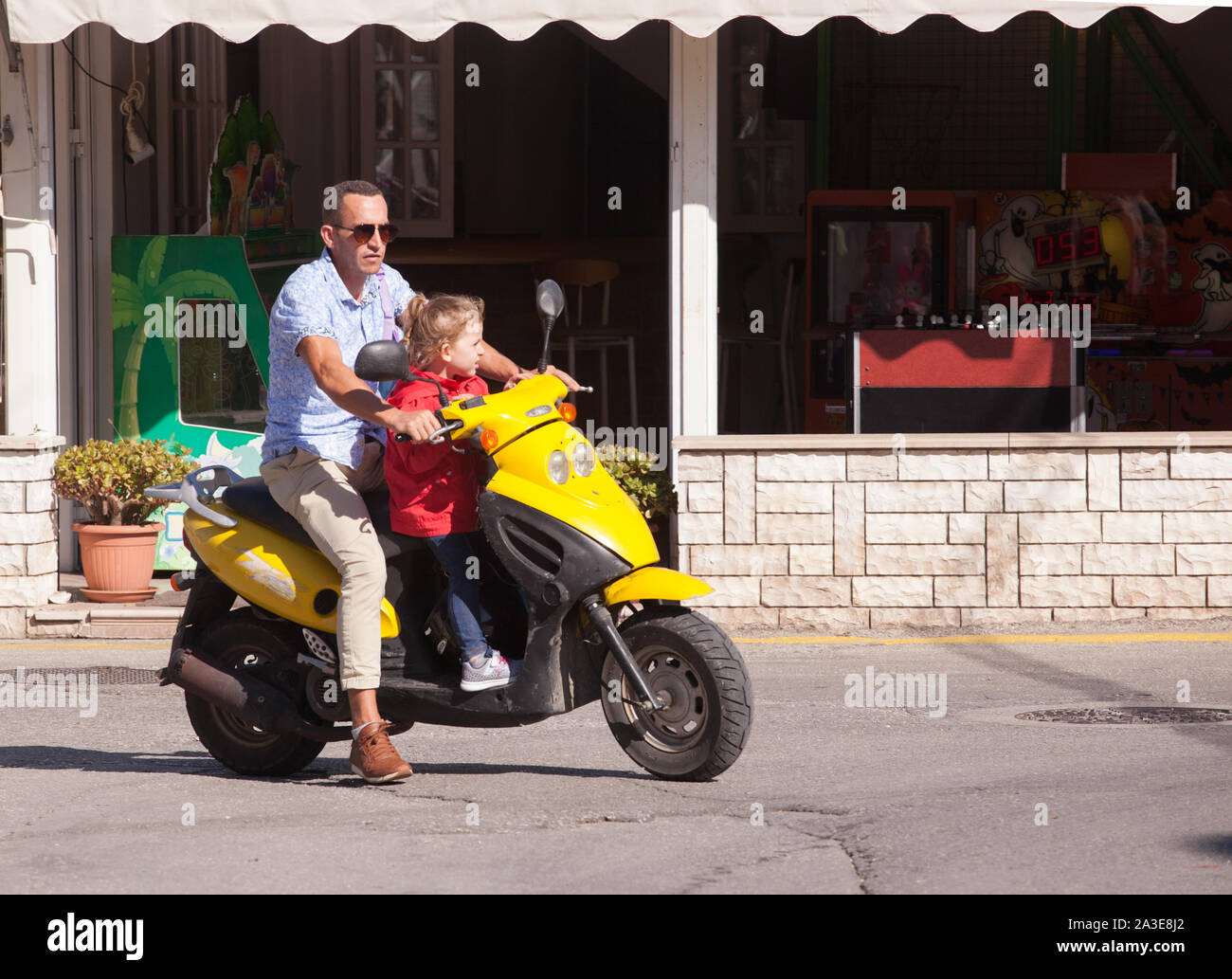 Mann, Motorroller ohne Sturzhelm und junge Kind ständigen durchlöcherte an den Lenker auf der Vorderseite von Scooter Stockfoto