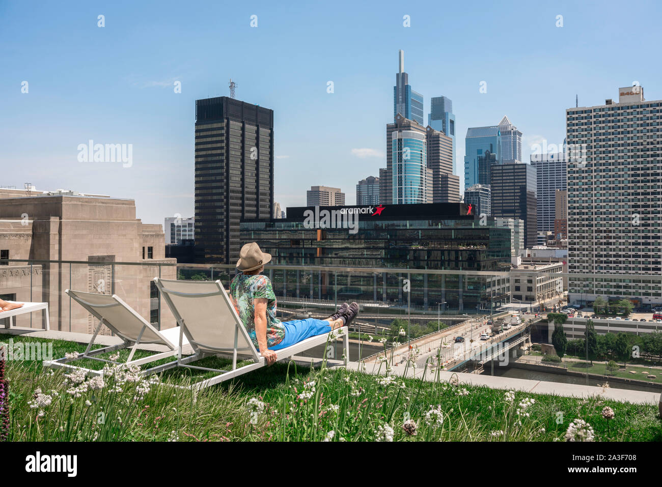 Downtown Philadelphia, Rückansicht eines Solo reife Frau am Philadelphia Skyline, sitzend auf einer Dachterrasse mit Liegestühlen, Pennsylvania, PA, USA Stockfoto