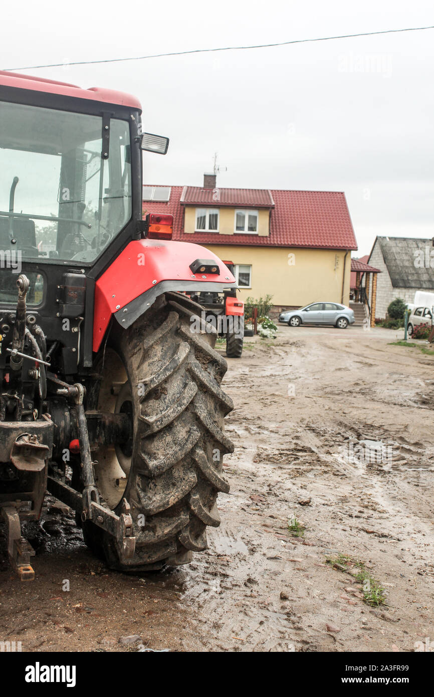 Rote Traktor im Hof eines Milchviehbetriebs. Ansicht von der Rückseite. Wohnung und Auto im Hintergrund. Podlasien, Polen. Stockfoto