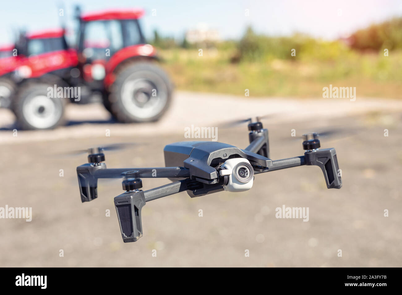 Kompakte schwarze Drone quadcopter mit Überwachungskamera tief fliegenden gegen rote landwirtschaftlichen Traktor Maschinen. Die Nutzung moderner Technologien und Stockfoto