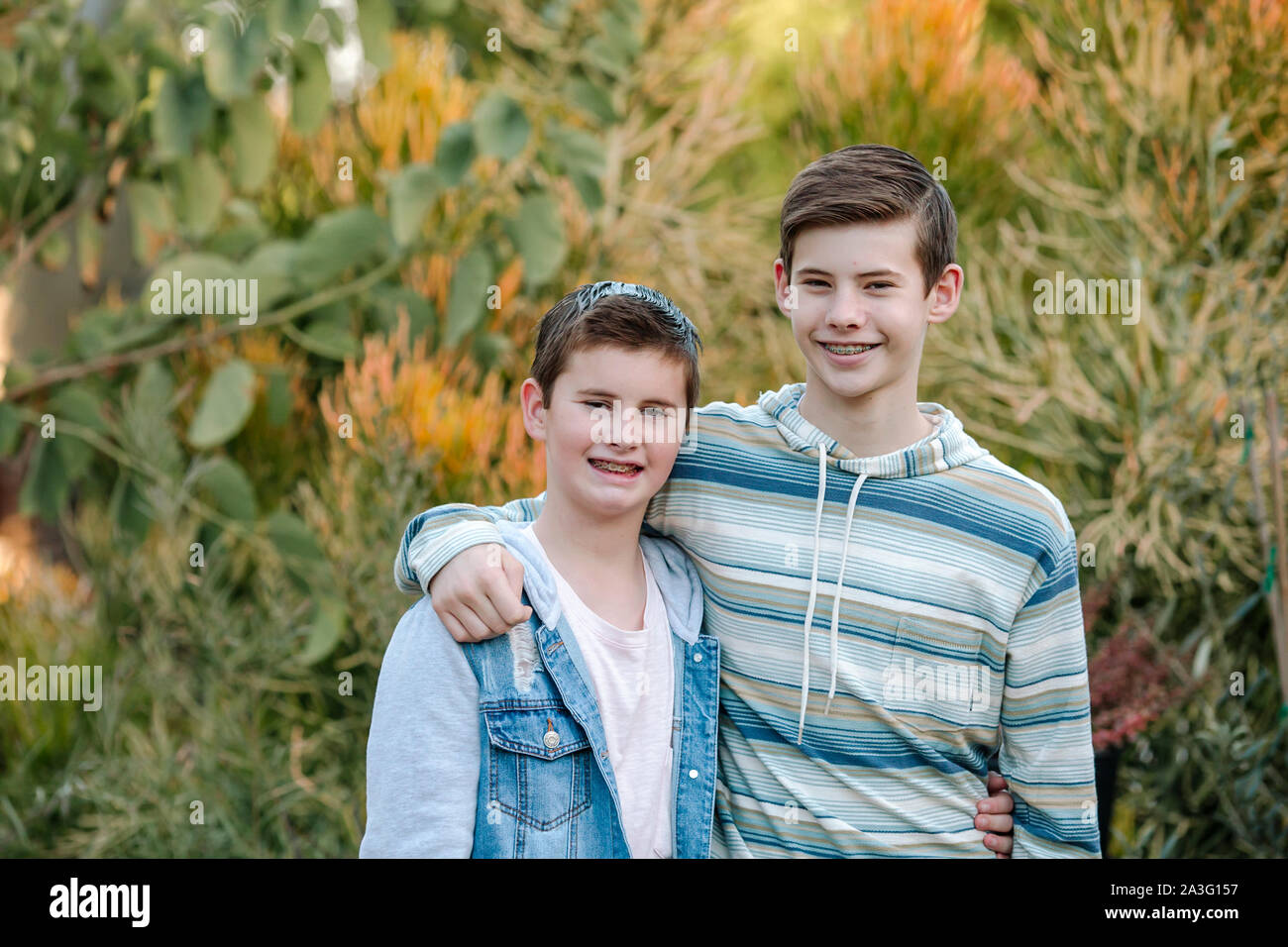 Saubere lächelnd Brüder mit Klammern umarmen vor üppigen Pflanzen Stockfoto