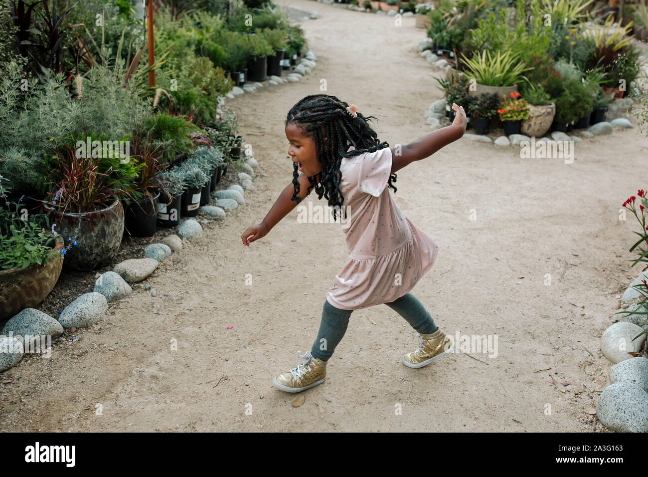 Süße junge schwarze Mädchen mit langen Zöpfen tanzen auf Garten Pfad Stockfoto