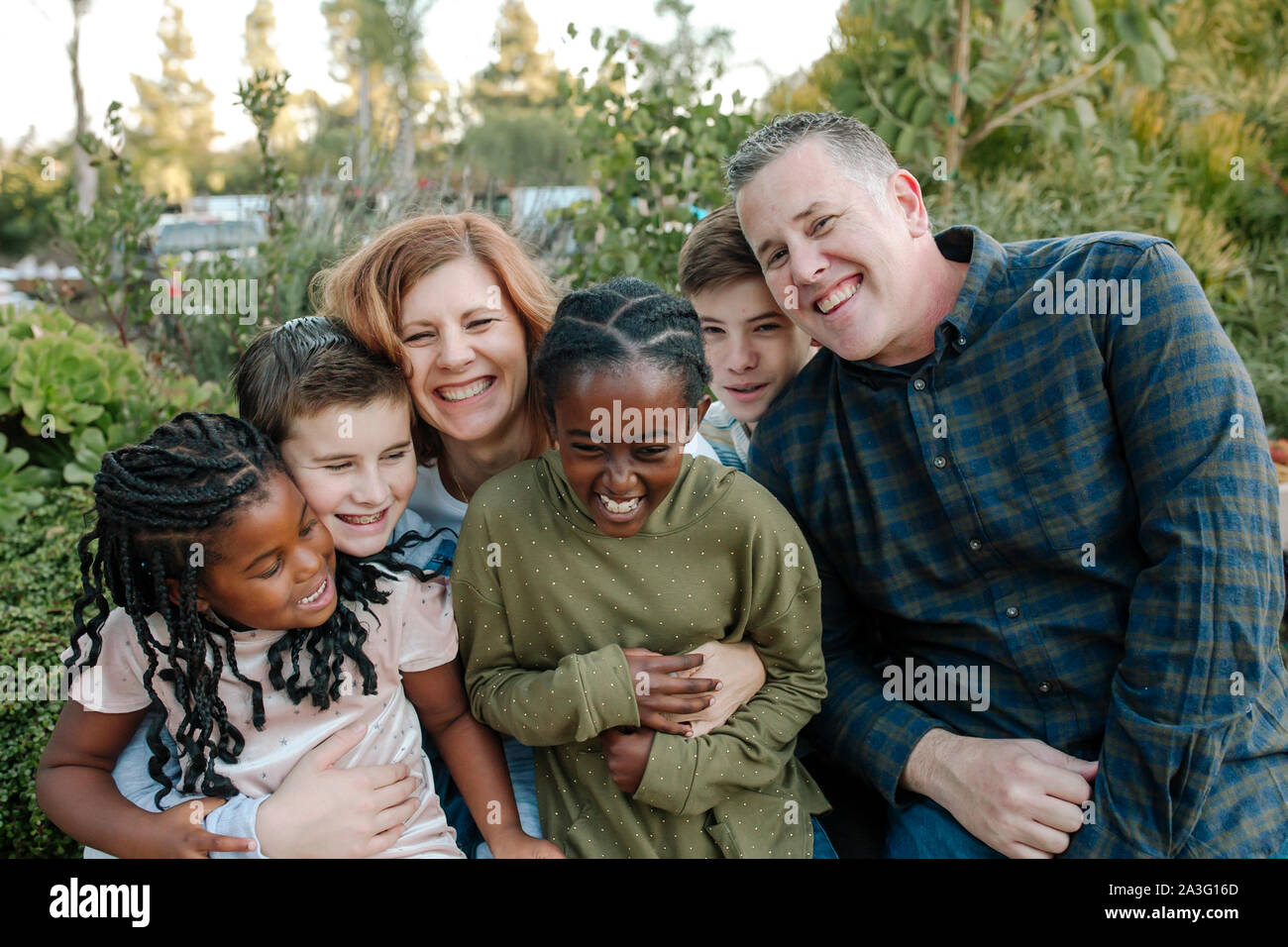 Lachend multirassischen Familie umarmen im Freien, umgeben von Pflanzen Stockfoto