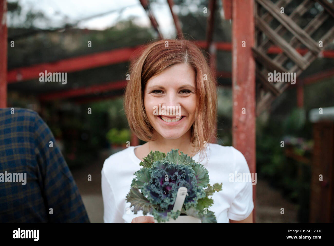 Lächelnd die Mitte-40 Frau mit roten Haaren holding Beetpflanze im Kindergarten Stockfoto