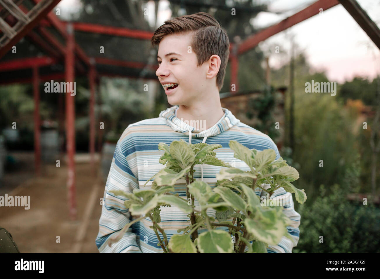 Lachend jugendlich Junge mit Zahnspange und kurze Haare holding Landschaft Anlage Stockfoto