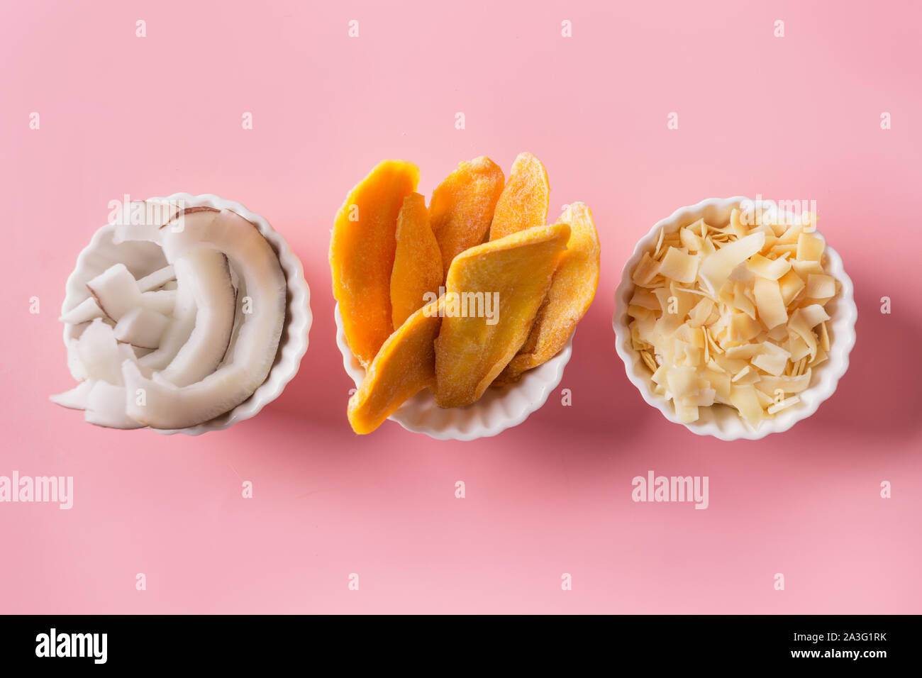 Entwässert und getrocknet Mango und Kokos Chips in weiße Schüssel auf rosa Hintergrund. Blick von oben. Stockfoto