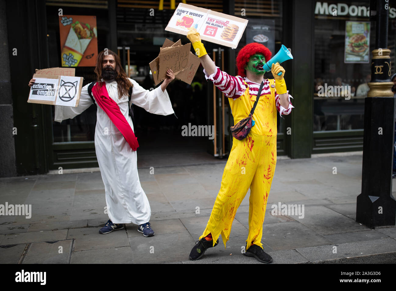 Die Demonstranten gekleidet, wie Jesus und Ronald McDonald außerhalb ein McDonald's Restaurant in der Nähe des Trafalgar Square, London, während ein Aussterben Rebellion (XR) Klimawandel protestieren. Stockfoto