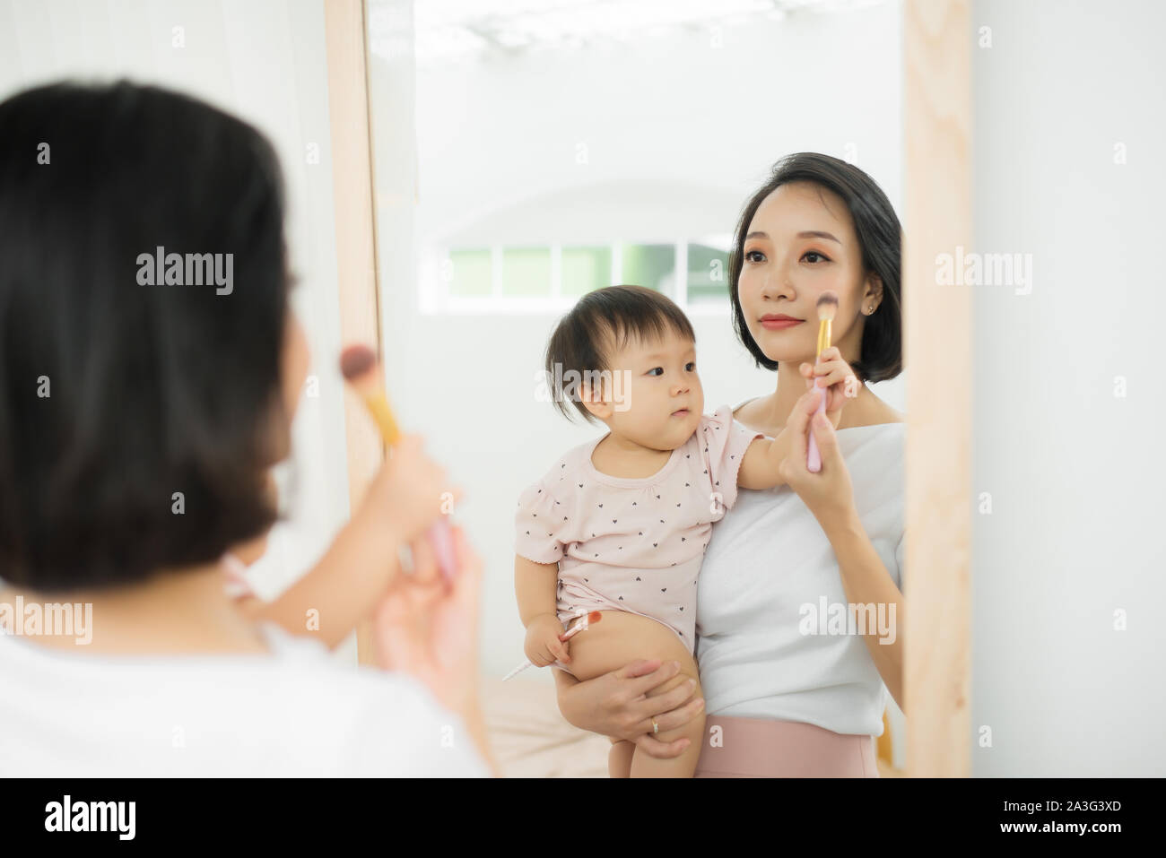 Lustige Familie zu Hause. Mutter und Kind Mädchen tun Sie Ihr Make-up und Spaß haben in der Nähe von Spiegel. Baby Mädchen erforscht die Mutter Kosmetik zu Hause Stockfoto